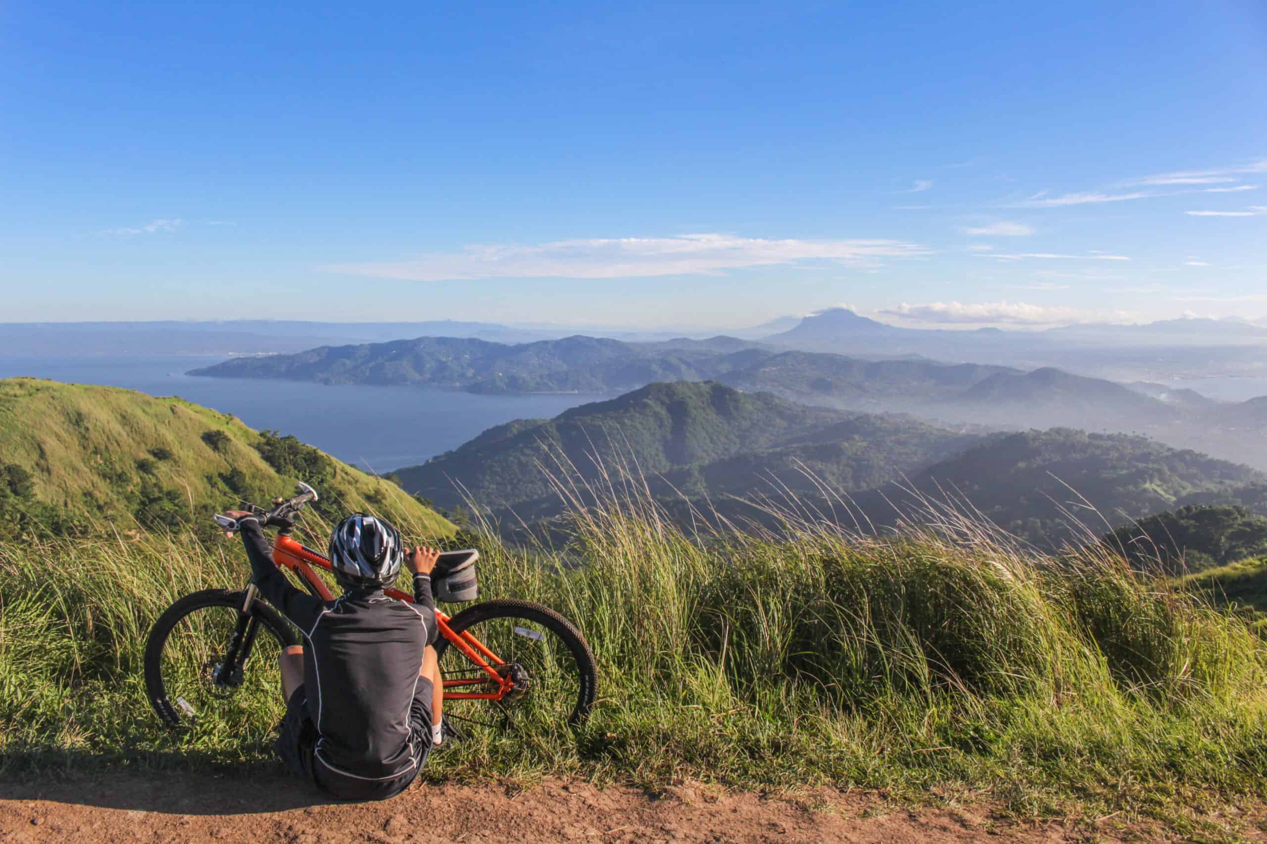 A picture of a cyclist sitting by their bike, taking in the moutaineous views