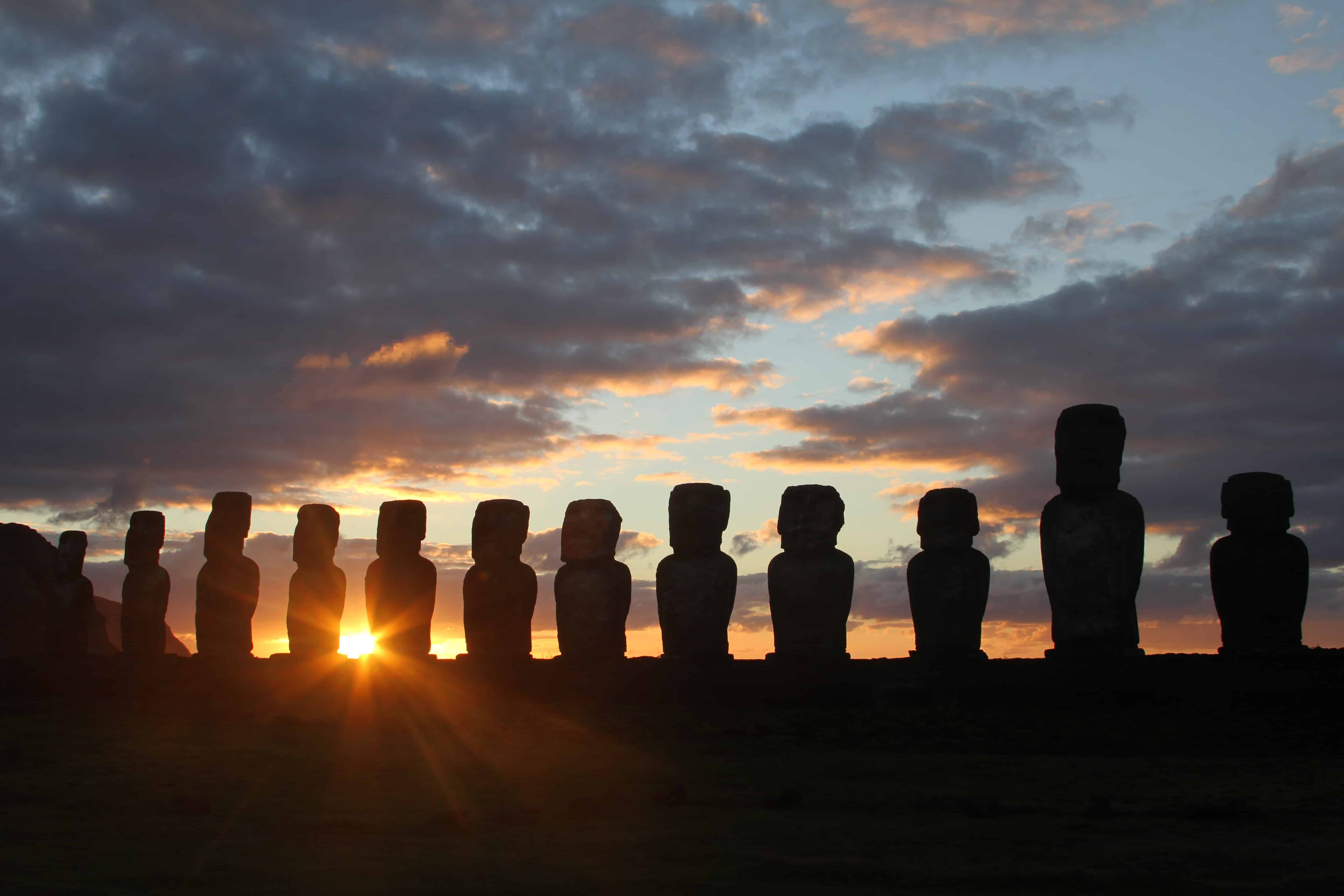 A line of 12 moai in a row with the sun setting in the background