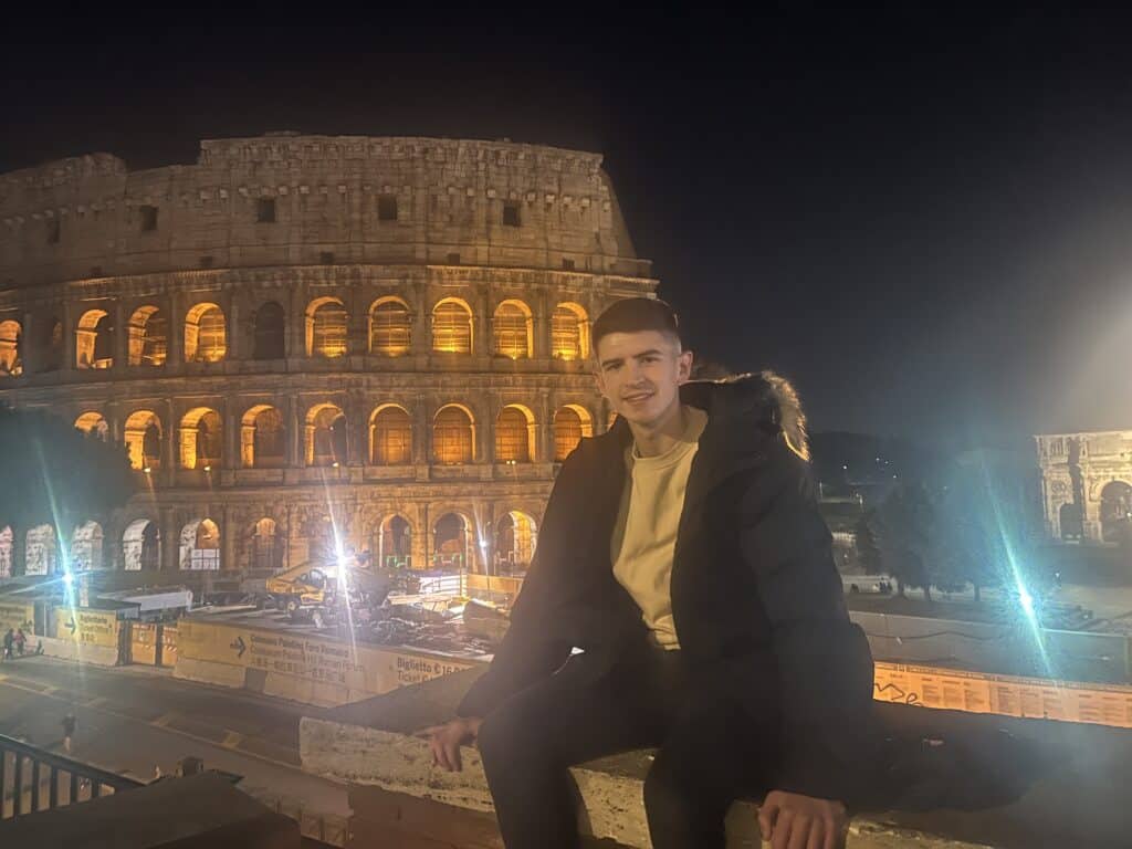 A picture of me sitting on the wall outside the Colosseum at night