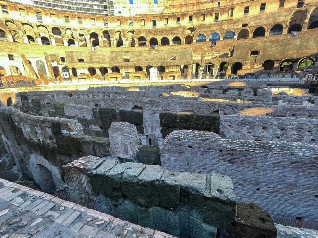 Close-up view of the Colosseum's underground structures, revealing the intricate network of walls and passageways, with the iconic tiers of seating rising in the background.