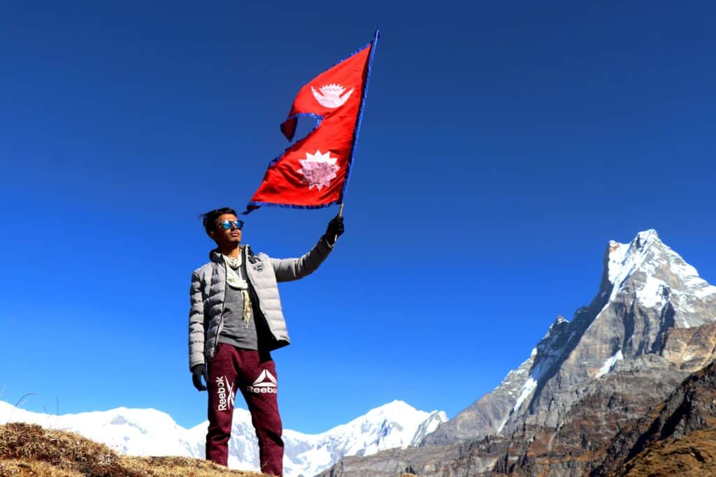 A picture of a person waving a Nepal flag in front of the Himalayas. Is Nepal in India? No. 