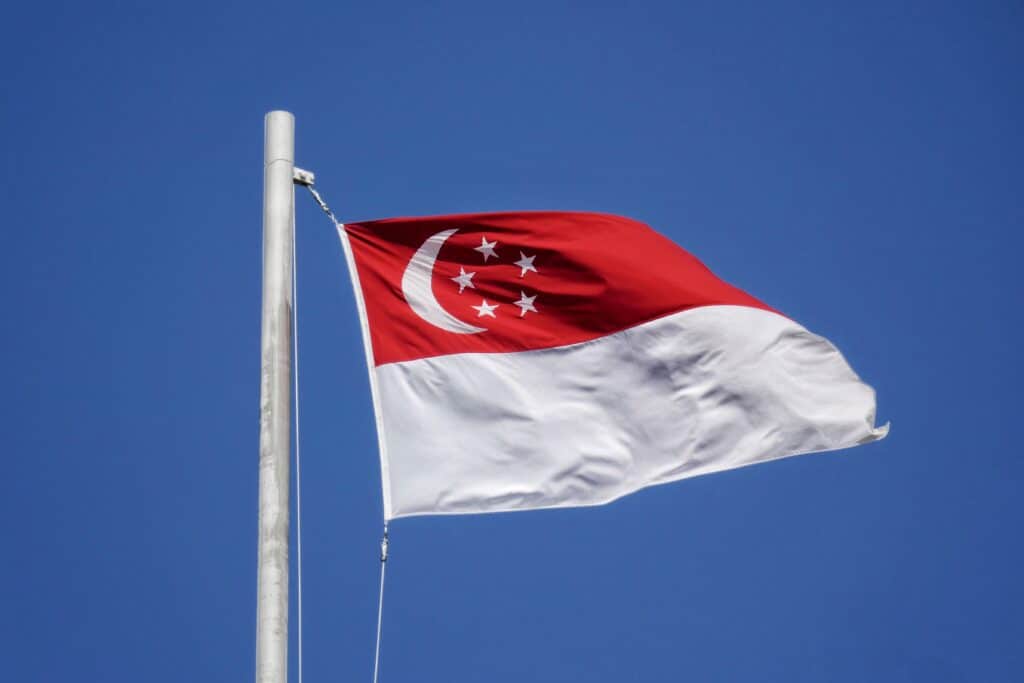 A picture of a flag of Singapore waving in front of a blue sky. 