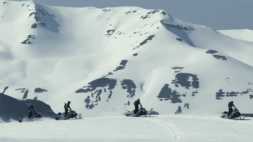 A picture of a group of snowmobiles driving past a snowcapped mountain during an Iceland snowmobile tour. 