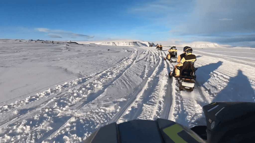 A picture taken from a snowmobile where you can see other snowmobiles ahead as they drive through the snow.