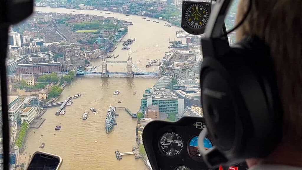 Aerial view of Tower Bridge in London with boats on the Thames River, seen from a helicopter tour.
