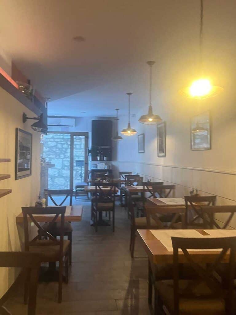 Dimly lit interior of Pizzeria Portas with empty wooden tables and pendant lighting fixtures.