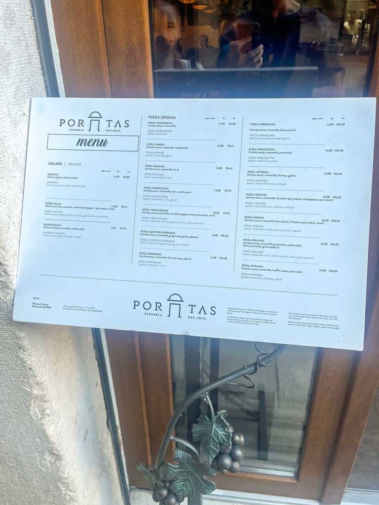 Close-up view of Pizzeria Portas menu displayed outside the restaurant, featuring a variety of pizzas and salads with prices in euros.