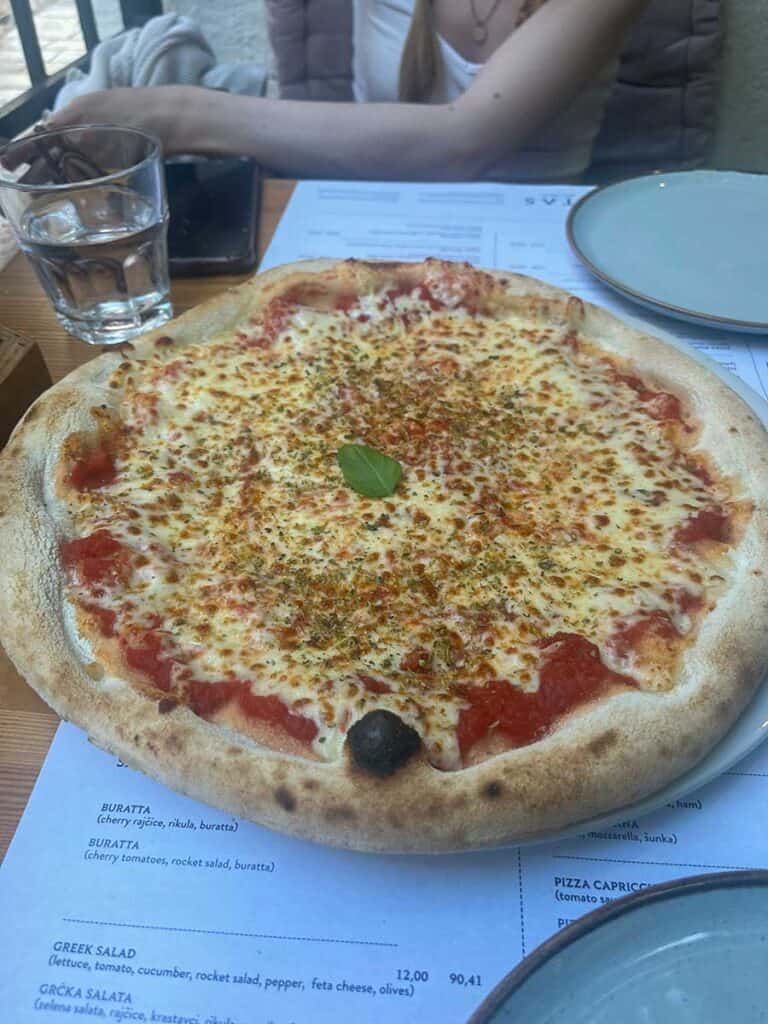 Freshly baked pizza with a golden crust and melted cheese on a white plate over a restaurant menu on a wooden table.