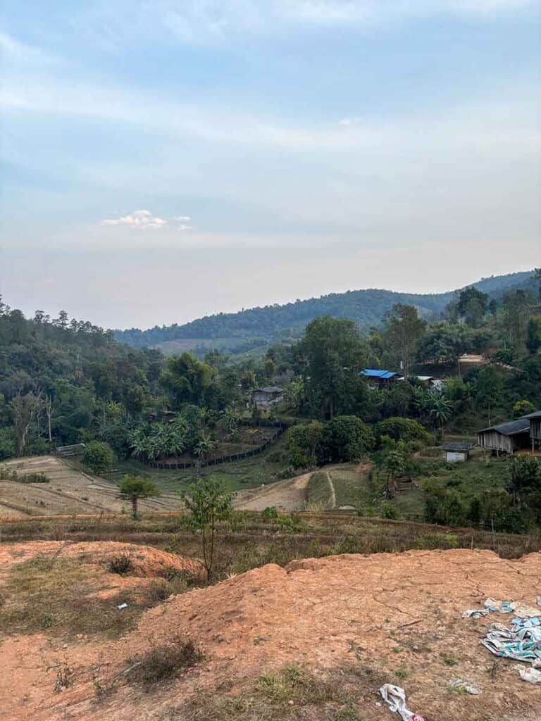 A panoramic view of a hilly village in Chiang Mai with tropical vegetation and scattered houses, under a hazy sky