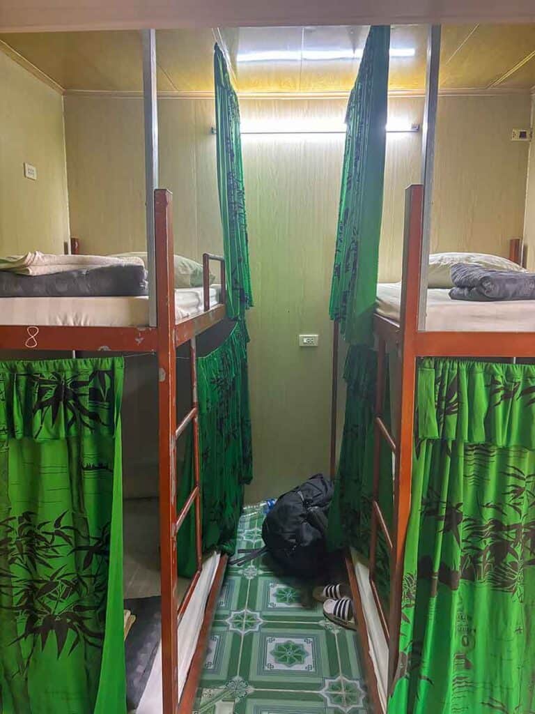 Inside view of a hostel dormitory with green curtains and wooden bunk beds in Tam Coc Riverside Homestay, Vietnam.