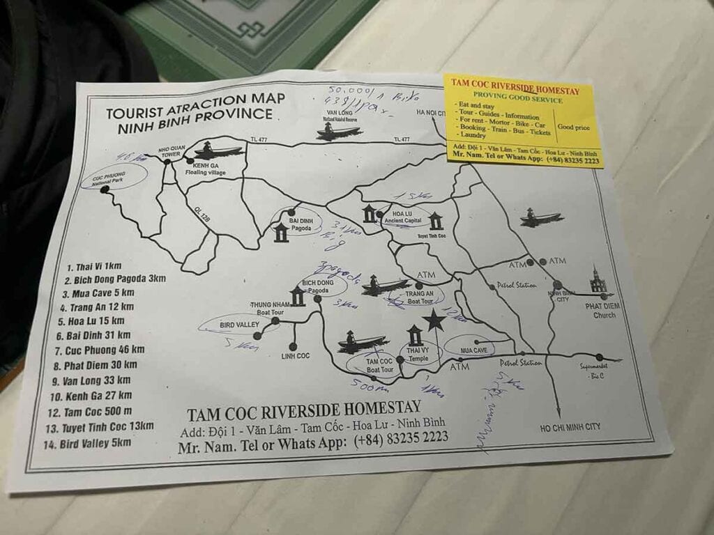 Handheld tourist map of Ninh Binh Province with various attractions like Mua Cave, Bai Dinh Pagoda, highlighted alongside a promotional sticky note for Tam Coc Riverside Homestay.