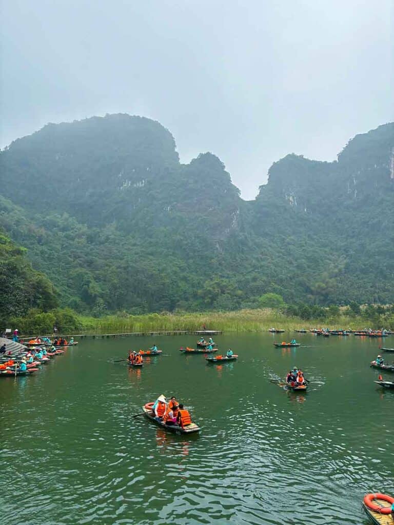 Tourists in orange life vests enjoy a boat ride through the scenic river flanked by lush green karst mountains in Trang An, Ninh Binh.